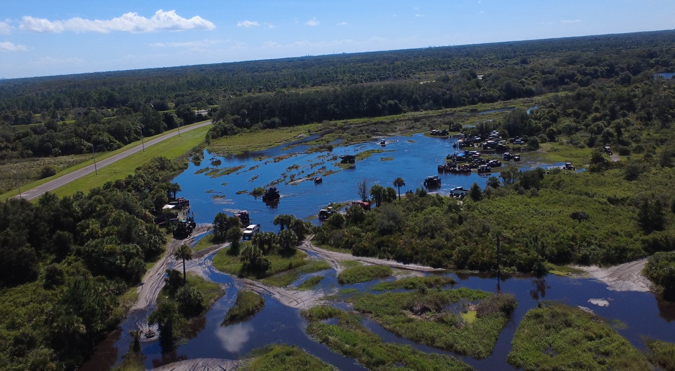 Wide aerial view of off-road trails and vehicles around a flooded area